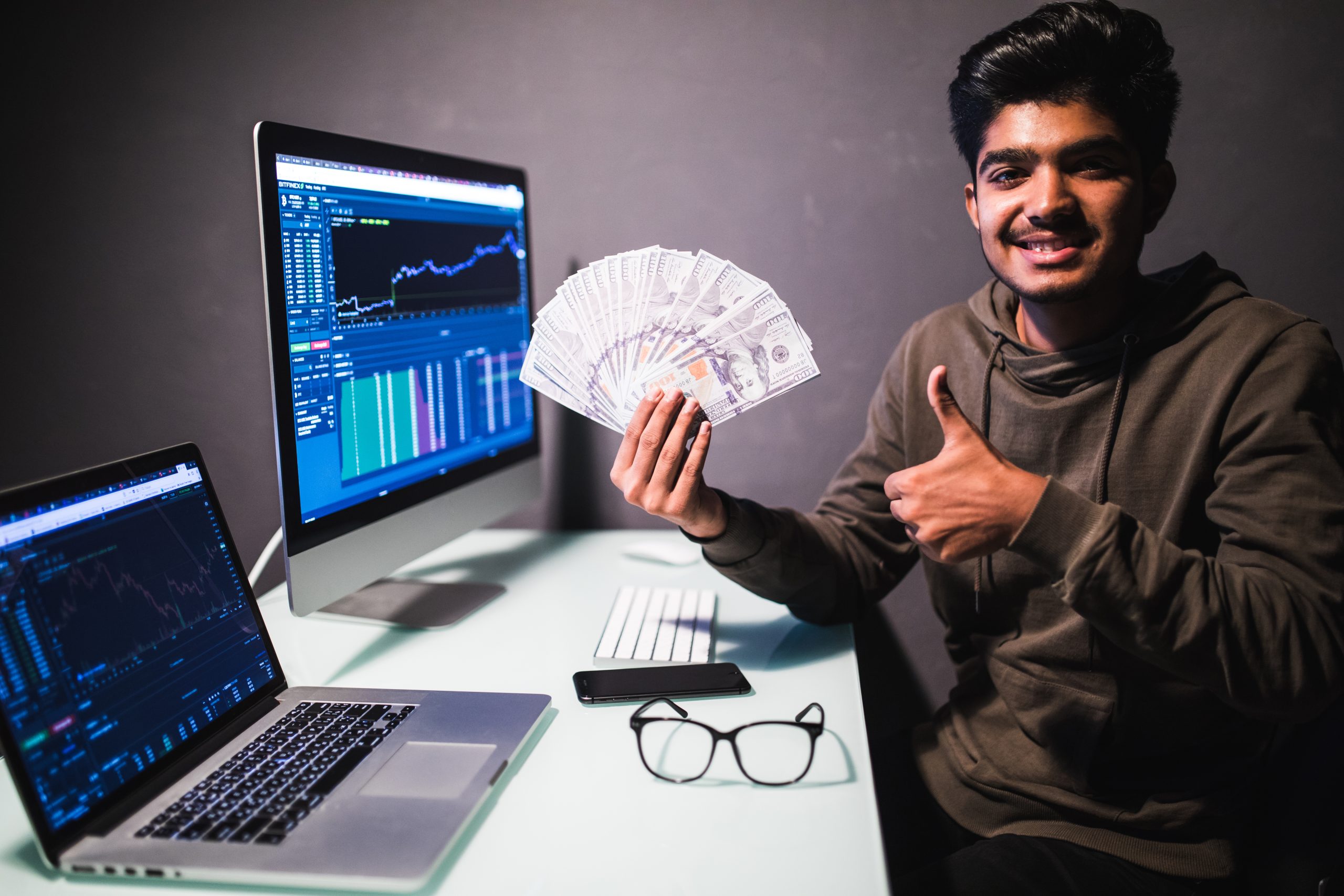 Angelic rich businessman with nimbus on head pointing dollar banknotes, encouraging to earn on internet, sitting at laptop workplace. indoor studio shot isolated on white background